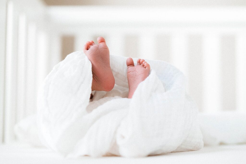 Newborn baby wrapped in a white muslin cloth laying in a white crib in his Frisco TX home