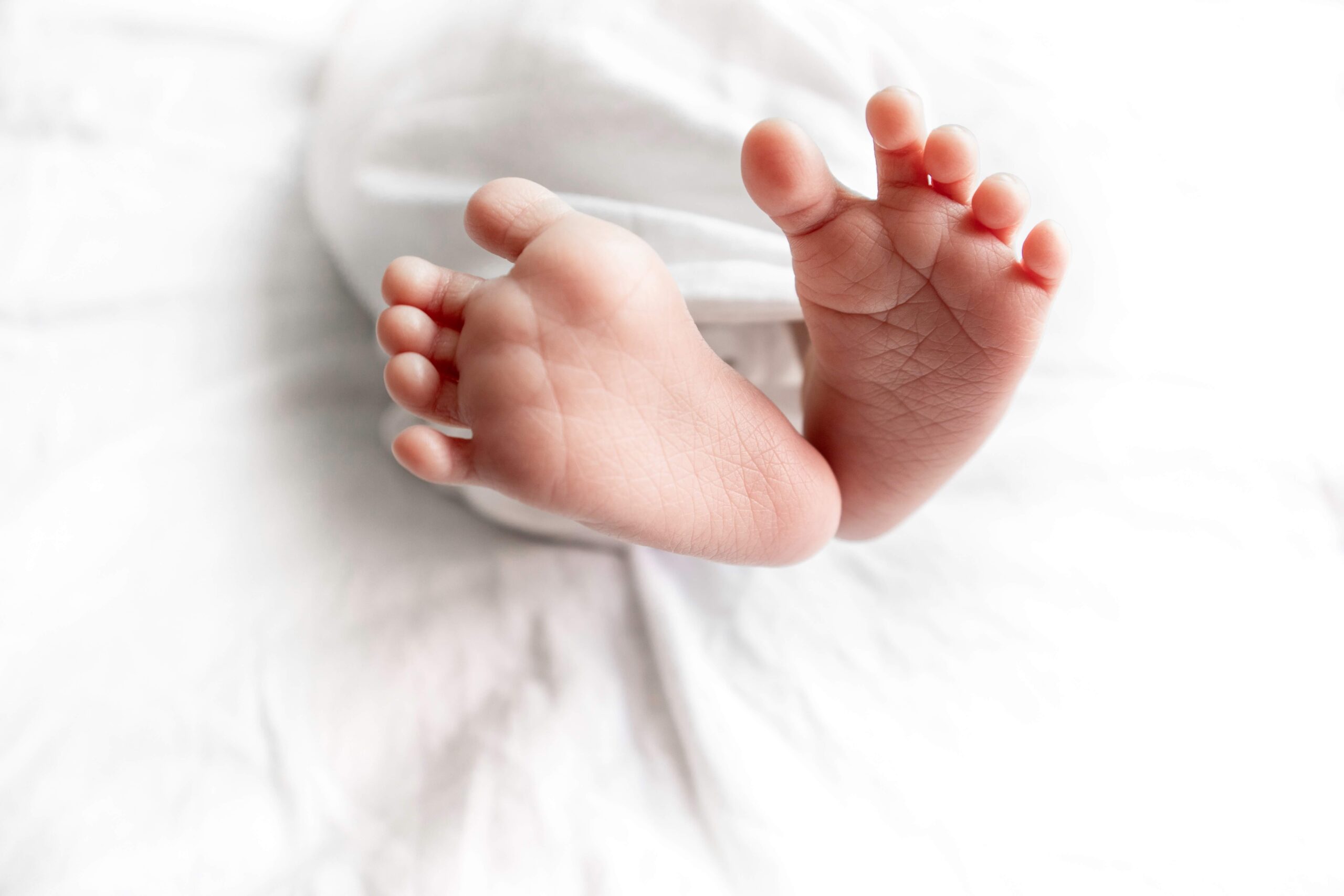 Sweet newborn baby feet wrapped in white bed sheet