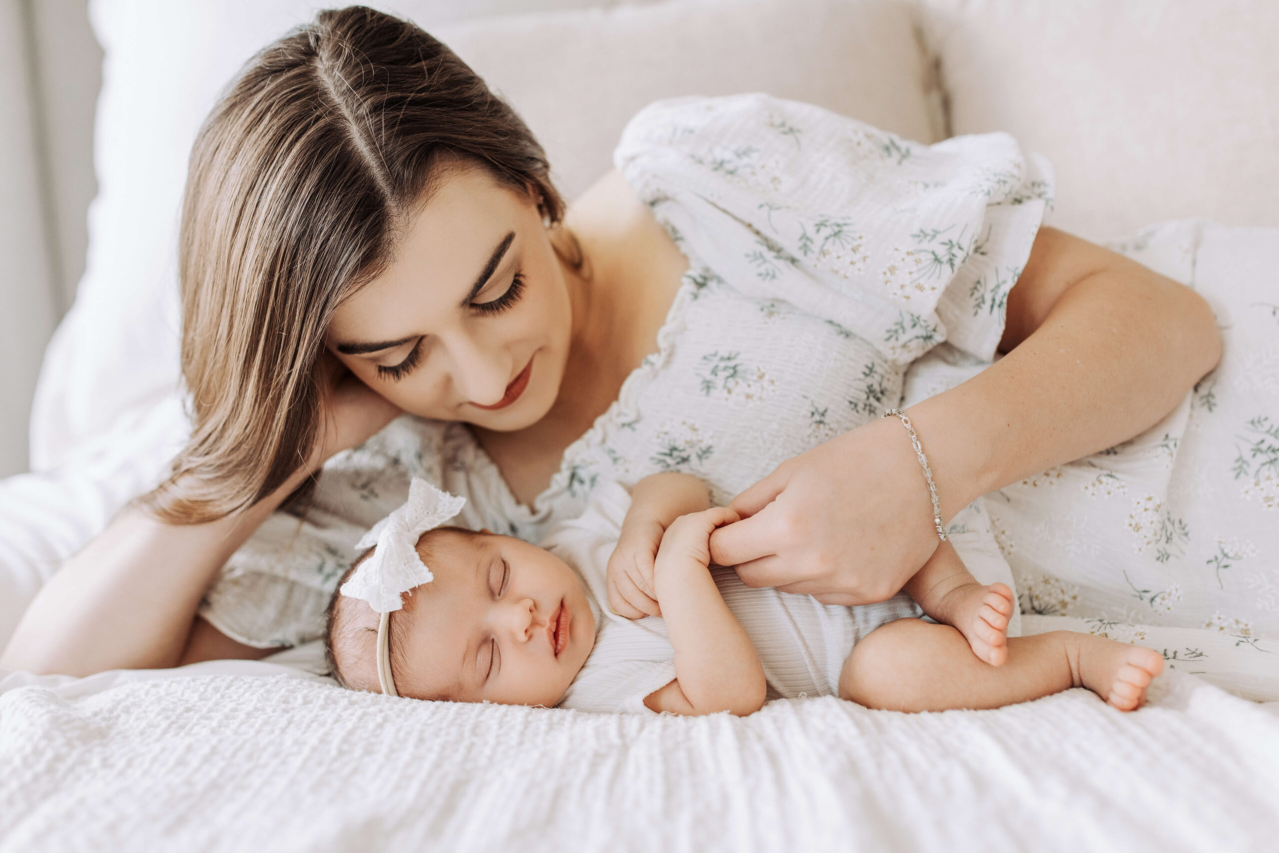 McKinney Mom looks down at her newborn lovingly in a bright. airy McKinney bedroom